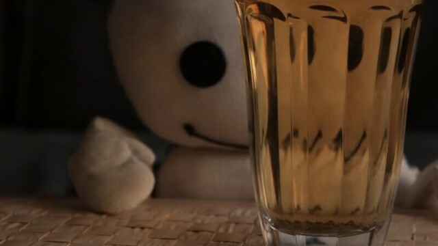 Das Wesen sieht mit einem Auge durch ein Teeglas schauend auf dem Sofa. Dasrechte Auge wird mehrfach reflektiert.