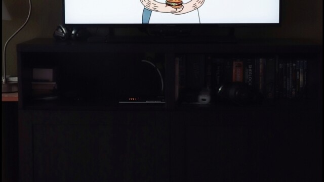 Das Wesen sitzt auf dem Boden vor dem oben auf dem Fernsehschrank stehenden Fernsehgerät. Es läuft gerade das Intro der Bobs Burgers Serie.
