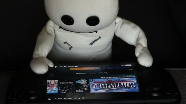 Das Wesen hat vor sich auf der Sofalehne ein Steamdeck liegen. Dort schaut es sich neugierig die darauf installierten Spiele an.