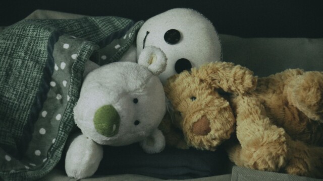 Gemeinsam kuscheln und eine Gutenachtgeschichte zur Begleitung. Das Wesen, hinten im Bild, Polst vorne links und Wilbur vorne rechts liegen zusammengekuschelt im Bett und lauschen einer Gutenachtgeschichte.